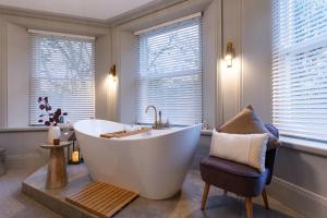 a bathroom with a tub and a chair and windows at Calming Crescent in Buxton