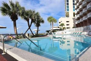 a swimming pool with palm trees and a building at Palmetto Beachfront Hotel, a By The Sea Resort in Panama City Beach