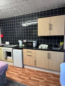 a kitchen with wooden cabinets and a black tiled wall at On The Beach Apartments in Blackpool