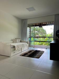 a white bedroom with a bed and a large window at Apartamento Villas do Pratagy in Maceió