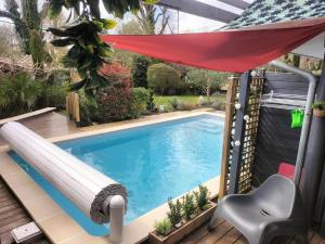 a swimming pool with a red umbrella and a chair next to it at Au bord du vieux Moulin in Mérignac