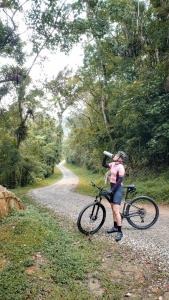 une femme tenant un vélo sur un chemin de terre dans l'établissement Pousada Vilarejo do Quim, à Tapiraí