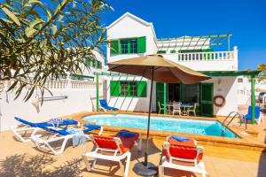 uma piscina com cadeiras e um guarda-sol e uma casa em Villa Alegranza em Puerto del Carmen