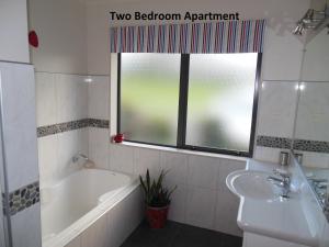 baño con bañera, lavabo y ventana en Silverdale Garden Stay, en Orewa