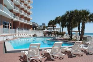 einen Pool mit weißen Stühlen und dem Meer in der Unterkunft Palmetto Beachfront Hotel, a By The Sea Resort in Panama City Beach