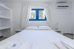 a white bedroom with a large white bed with a window at Skinopi Beach Guesthouse in Schinopi