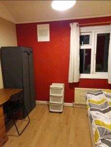 a room with a red wall with a bed and a desk at Welcoming Home Close to Transport Links in Thornton Heath