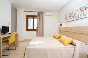 1 dormitorio con cama con almohadas amarillas y escritorio en Hotel La Perdi, en Sant Mateu