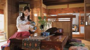 Uma mulher está sentada numa sala a beber de um copo. em 大正の宿　浪漫邸 em Kani