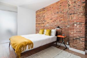 ein Schlafzimmer mit einer Ziegelwand und einem Bett mit gelben Kissen in der Unterkunft Le Merrill Boutique Hotel in Montreal
