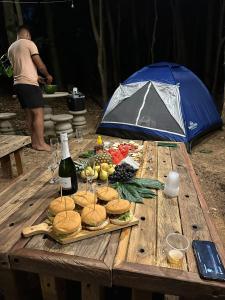 una mesa de picnic con sándwiches y una botella de vino en Espaço camping -Barraca 3, en Itapira