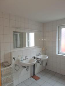 a white tiled bathroom with two sinks and a mirror at Gasthof Hirschkeller in Göppingen