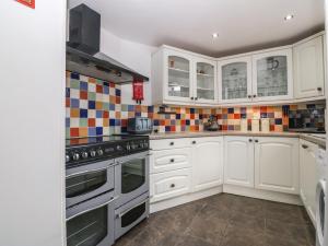 a kitchen with white cabinets and tiles on the wall at Platform 13 Railway Cottage in Llandudno Junction