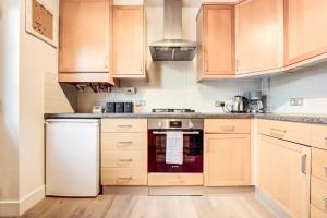 a kitchen with wooden cabinets and a white dishwasher at Bright Charming Apartment In Ealing in London