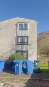 drie blauwe vuilnisbakken voor een gebouw bij Budget Rooms in Fort William