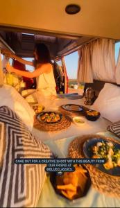 Uma mulher sentada na traseira de uma carrinha com comida. em Rent a Blue Classics' s Campervan for your Road trip in Portimao -VOLKSWAGEN T3 em Portimão