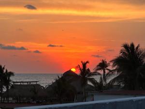 a sunset on the beach with palm trees and the ocean at Hotel Casa Prisca in Coyuca