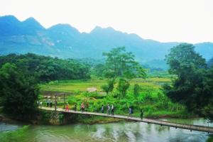 un grupo de personas caminando a través de un puente sobre un río en Puluong homestay nacoLodge, en Làng Chiêu