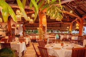 un restaurante con mesas y sillas blancas y palmeras en Nosy Be Hotel & Spa, en Ambondrona