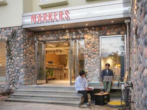 two men sitting outside of a marriott building at Markers Hostel in Gangneung