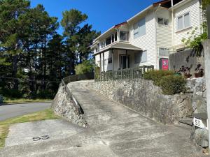 a white house with a stone retaining wall next to a street at BBs B&B in Lower Hutt