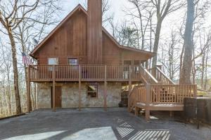 a large wooden house with a deck in the woods at Dudley II by AvantStay Comfortable Cabin w Hot Tub Views in Pigeon Forge
