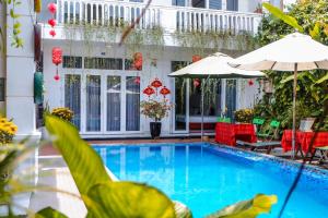 a pool with red chairs and umbrellas next to a building at Oleander Garden Homestay in Hoi An