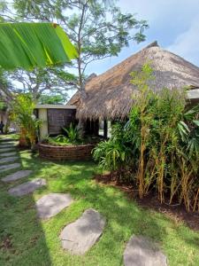 a house with a thatched roof and a grass yard at Lodge tropical Fullmoon in Uluwatu