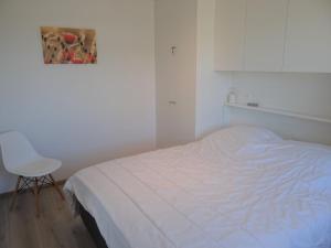 ein weißes Schlafzimmer mit einem Bett und einem Stuhl in der Unterkunft Karthuizer E1 located between the dunes in Nieuwpoort