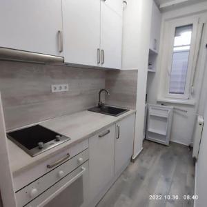 uma cozinha com armários brancos, um lavatório e uma janela em LBB apartman em Sátoraljaújhely