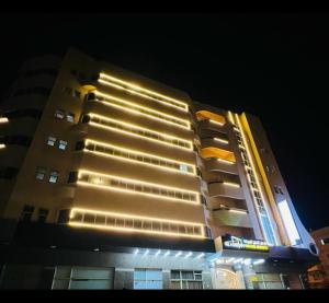 een hoog gebouw met 's nachts verlichting bij AL MARJAN FURNISHED APARTMENTS in Ajman 