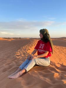 a woman sitting on the sand in the desert at Miostello Lifestyle Hostel Marrakech in Marrakech