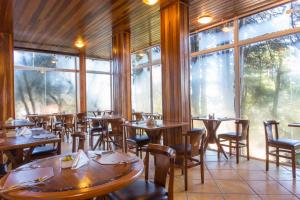 un restaurante con mesas y sillas de madera y ventanas en Pousada La Toscana Campos do Jordão, en Campos do Jordão