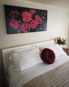 a bed with white pillows and a painting of roses at Warm little house at Wesley in Auckland