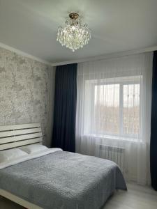 um quarto com uma cama com um lustre e uma janela em 3-комнатные Апартаменты LUX em Taraz