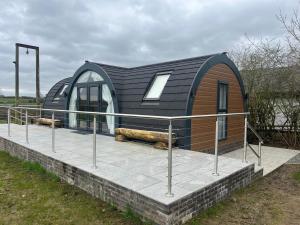 una pequeña casa negra con una terraza en un campo en The Pod @ Cold Comfort Farm en Hinckley