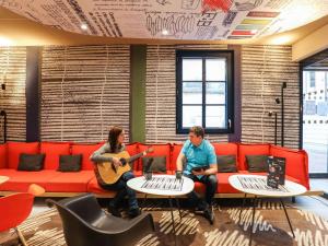 duas pessoas sentadas num sofá a tocar música em ibis Saint Germain en Laye Centre em Saint-Germain-en-Laye
