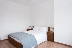 um quarto com uma cama com lençóis brancos e pisos em madeira em Paulo Guest Apartment nas Caldas da Rainha