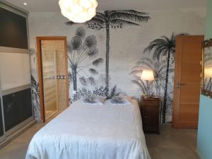 a bedroom with a white bed with palm trees on the wall at Belle villa, piscine et cigales au calme ! in Saint-Jean-de-Védas