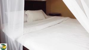 a bedroom with a bed with white sheets and curtains at Antique Apartments in Entebbe +3 photos