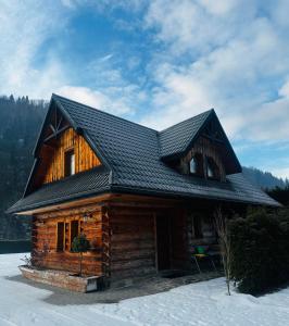 uma cabana de madeira com um telhado preto na neve em Nad Grajcarkiem em Szczawnica