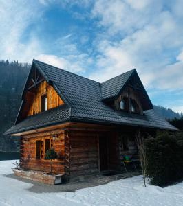 domek z bali z czarnym dachem w śniegu w obiekcie Nad Grajcarkiem w mieście Szczawnica