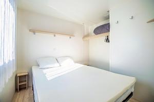 a small bedroom with a white bed and a window at Mobil-Home Valras plage in Valras-Plage