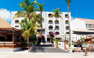 a large white building with palm trees in front of it at Holland House Beach Hotel in Philipsburg