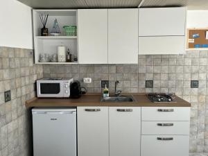 cocina con armarios blancos, fregadero y microondas en Casa Maruzzella, en Lipari