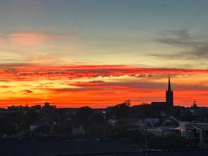 einen Blick auf den Sonnenuntergang über einer Stadt mit Kirchturm in der Unterkunft Moderne 3 Zimmer Wohnung in Heiligenhaus in Heiligenhaus