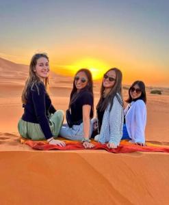 un grupo de mujeres sentadas en la arena en el desierto en Desert Berber Fire-Camp en Merzouga