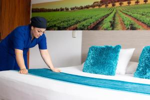 a woman putting a blue blanket on a bed at Hotel Portón Sabaneta in Sabaneta