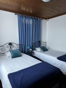 two beds in a bedroom with blue curtains at Alojamentos A Buraca in São Roque do Pico