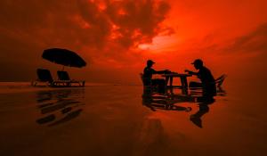 two people sitting at a table on the beach at sunset at Hide Inn Blue in Nilandhoo
